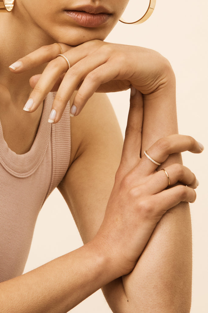 Detail view of models hands wearing Polished Gold Rings and Diamond rings on multiple fingers by Bagatiba
