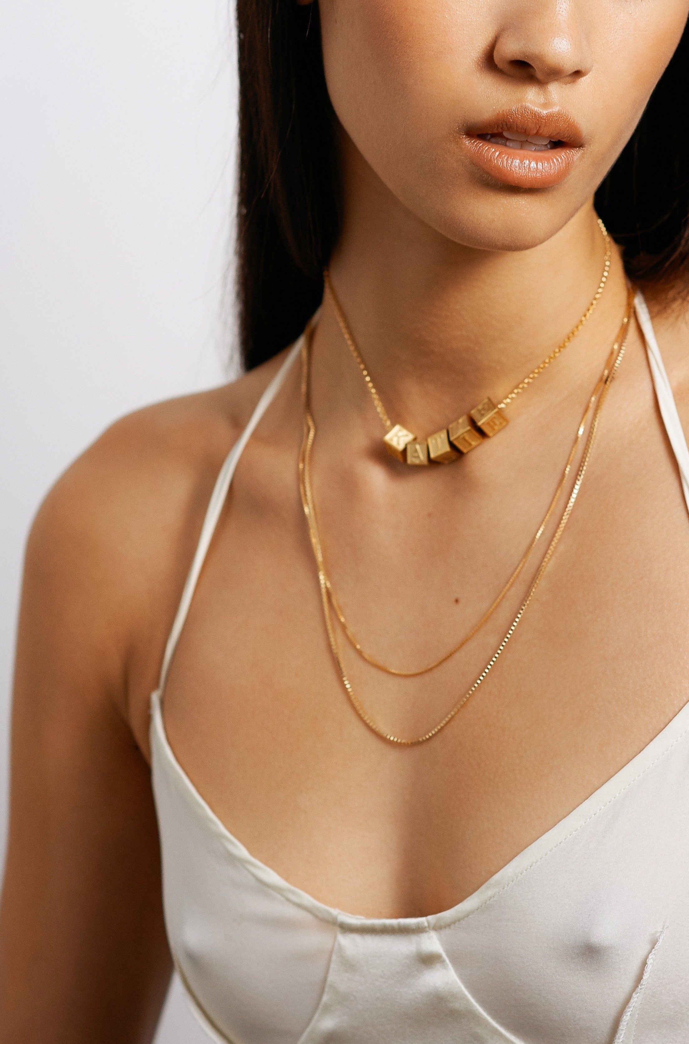 Model wearing 5 letter blocks on choker chain paired with two longer chain styles bagatiba