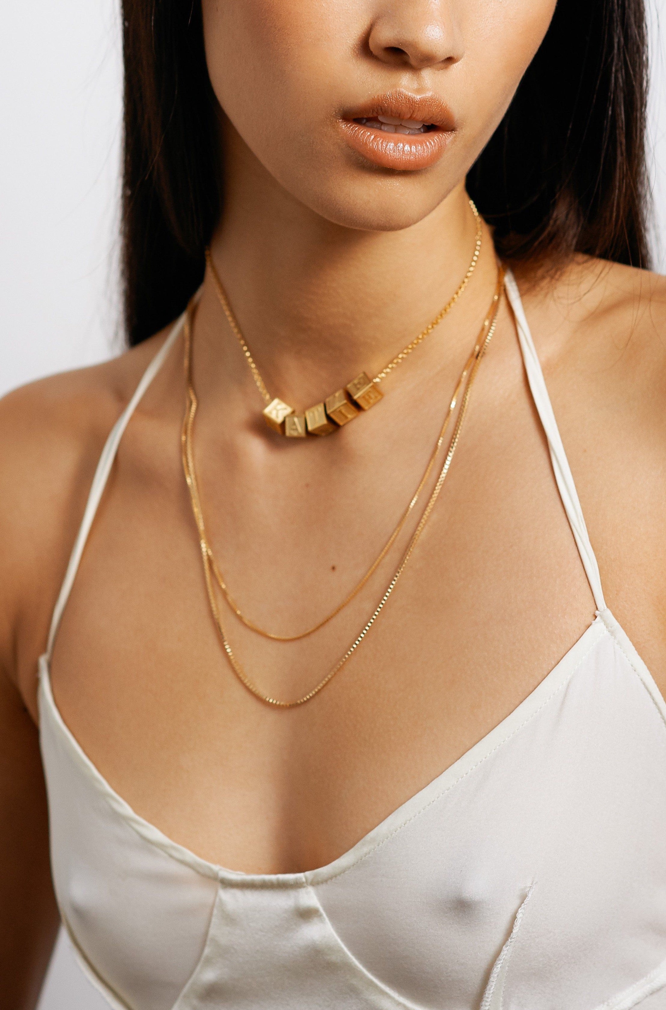 Model wearing 5 letter blocks on choker chain paired with two longer chain styles bagatiba