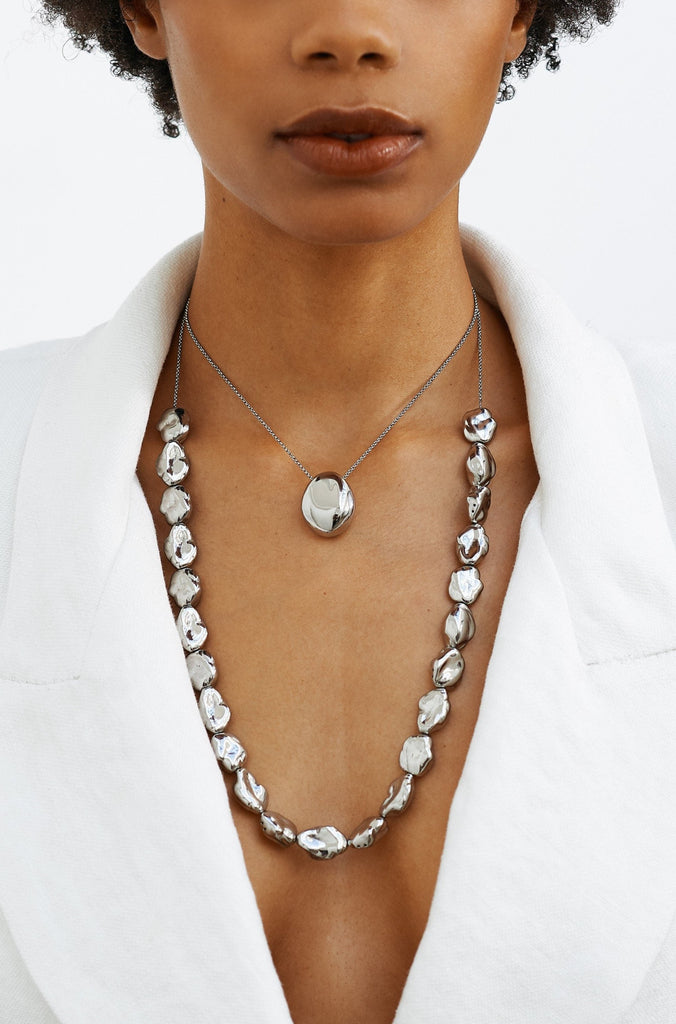 Model wearing the Silver Orb Necklace and Silver Pearl  Necklace by bagatiba Styled with a low cut white blazer